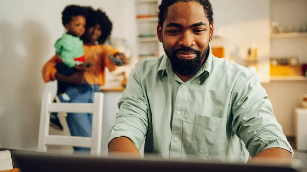 Man doing research for life insurance at his laptop while his family watching in the background