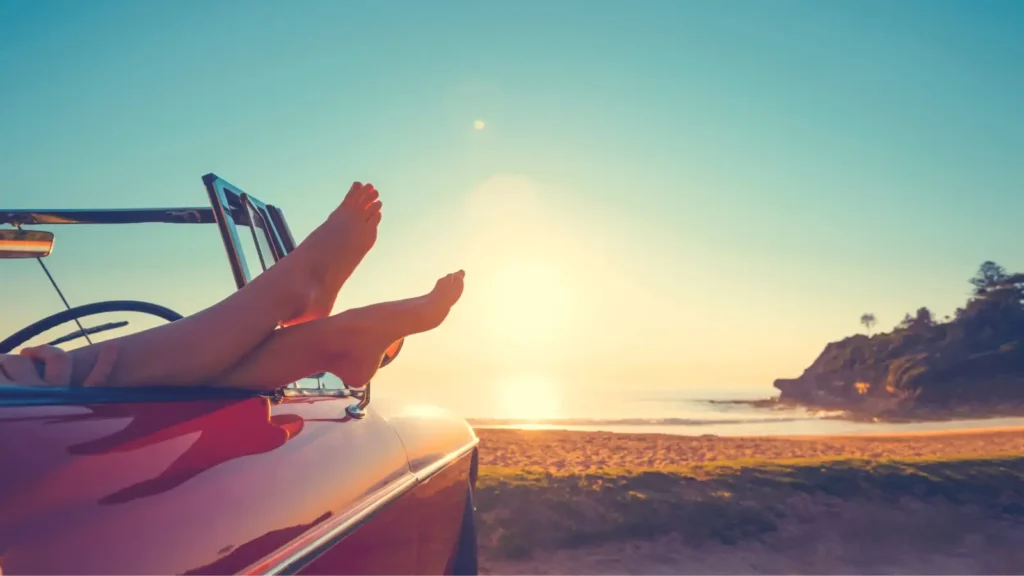 Feet dangling outside of a convertible car while watching the sunset on a beach